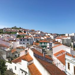 Weißes Dorf mit Terrakottadächern auf einem Hügel in Portugal. Traditionelle Häuser gruppieren sich an Hängen unter blauem Himmel.