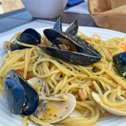 Plate of spaghetti with black mussels and white clams on a white plate in Cinque Terre, Liguria. A white bowl is visible in the background.
