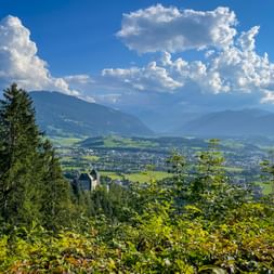 View from Kitzbühel Alps over Saalfelden valley with green meadows, mountains, and dramatic white clouds in blue sky.