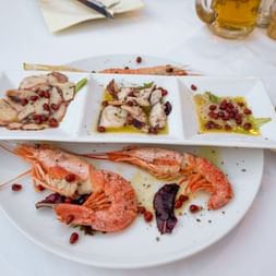 Seafood platter with grilled prawns and three portions of octopus garnished with pomegranate seeds and olive oil on white plates.