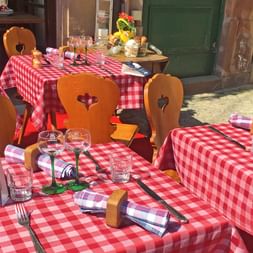 Restauranttische im Freien mit rot-weiß karierten Tischdecken und Holzstühlen mit Herz-Ausschnitten im Elsass, Frankreich.