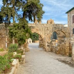 Antike Steinbögen und Ruinen in Famagusta, Zypern, mit Palmen und mediterraner Vegetation unter teilweise bewölktem Himmel.