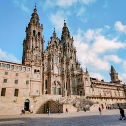 Kathedrale von Santiago de Compostela mit barocker Fassade und Zwillingstürmen. Menschen gehen über den Platz vor der historischen Kirche.