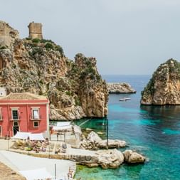 Bucht Scopello Malerischer Blick auf Scopello in Sizilien mit antiken Steintürmen auf Felsklippen, türkisfarbenem Mittelmeer und bunten Gebäuden mit rotem Haus.