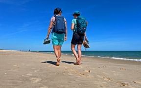 Hikers walk barefoot across the beach on Ilha de Tavira