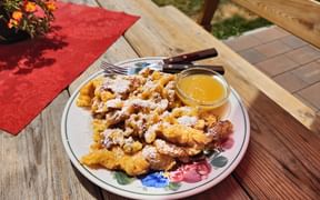 Plate of Kaiserschmarrn dusted with powdered sugar and served with applesauce on a wooden table with red napkin and flowers.
