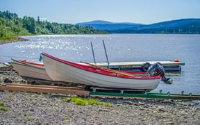 Weißes Motorboot mit rotem Rand auf einem Anhänger am Seeufer in Funäsfjällen. Berge und Wälder über dem glitzernden Wasser sichtbar.