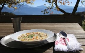 Schüssel traditionelle italienische Gerstensuppe mit Gemüse auf Holztisch im Freien mit Berglandschaft im Hintergrund.