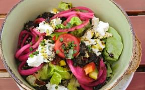 Fresh salad bowl with lettuce, white sheep cheese, pink pickled onions, tomato, olives, and herbs in a ceramic bowl.