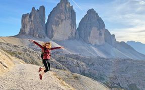 Hiker in the Dolomites, jumps and stretches her arms out to the side, sunshine