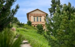 Königshaus am Schachen, ein beiges Holzgebäude mit erhöhtem Balkon, umgeben von grünen Bergkiefern und Almwiese entlang eines Schotterwegs.