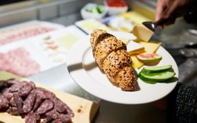 Frühstücksauswahl mit Körnerbrötchen, Käsescheiben, Gurke, Tomate und Aufschnitt auf weißen Tellern im Hotel Continental Park, Luzern.