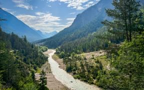 Breites Flusstal mit flacher Isar, die durch bewaldete Hänge fließt. Berge erheben sich beiderseits unter teilweise bewölktem Himmel bei Scharnitz.