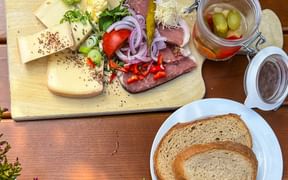 Wooden platter with cheese, cured meat, vegetables, and pickles alongside bread slices on a rustic table in Lechaschau.