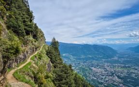 Bergweg am Meraner Höhenweg entlang eines steilen Hangs mit Panoramablick auf Meran und das Tal in Südtirol.