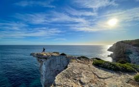 Einsamer Wanderer auf dramatischer weißer Kalksteinklippe bei Ses Piquetes an Mallorcas Ostküste mit Blick auf türkises Mittelmeer unter sonnigem Himmel.