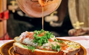 Caldo de peixe wird aus einem Tontopf auf Brot mit weißem Fisch und frischen Kräutern auf einem braunen Teller auf den Azoren geschöpft.