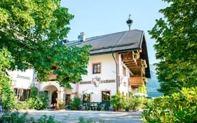 Traditional Austrian Seehotel Huber with white walls, wooden balconies, and red shutters surrounded by lush green trees and gardens.