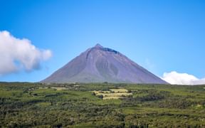 Ponta do Pico, ein kegelförmiger Vulkanberg auf den Azoren, der sich über grüne landwirtschaftliche Felder und Vegetation unter blauem Himmel erhebt.