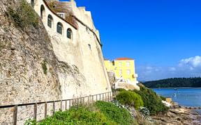 Historische weiße Schlossmauern von Vila Nova de Milfontes auf Felsklippen über Sandstrand und blauem Ozean unter klarem Himmel.