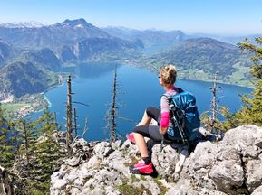 Frau in Wanderbekleidung sitzt auf einem Felsen mit Blick auf Seen und Berge