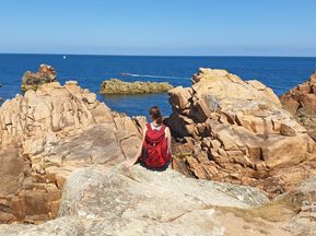 Wanderer genießt den tollen Ausblick auf die roten Granitfelsen und das Meer