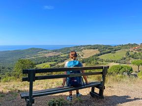 Wanderin sitzt auf Bank mit hügeliger Landschaft im Hintergrund