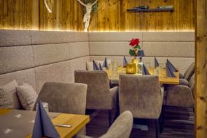 Restaurant dining area with wooden walls, upholstered seating, and set tables with purple napkins. A crucifix and decorative elements adorn the wall.