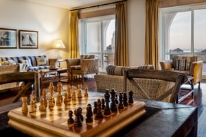 Helle Lounge im Hotel Pousada Sagres mit Korbmöbeln, Schachbrett, gestreiften Kissen und großen Fenstern mit goldenen Vorhängen.