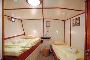 Compact ship cabin on MS Sagena with two single beds, cream bedding, wooden trim, nightstand, round stool, and ceiling light.