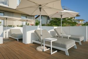 Moderne Hotelterrasse im Palazzo del Garda mit grauen Sonnenliegen, weißen Sonnenschirmen und Holzdecking mit Blick auf Wohngebäude.