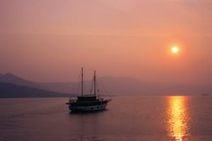 MS Dalmatino cruise ship anchored on calm waters during sunset with golden light reflecting on the sea and mountainous coastline in background.