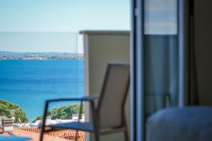 Blick vom Balkon des Hotel Palazzo del Garda auf das blaue Wasser des Gardasees, entfernte Küstenlinie und Balkonstuhl im Vordergrund.