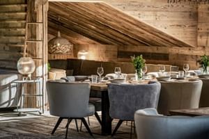 Modern alpine restaurant with wooden walls, set dining table with wine glasses, upholstered chairs, and decorative lighting at Sepp Hotel Maria Alm.