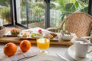 Frühstück mit frischen Orangen, Orangensaft, Kaffee und verschiedenen Gebäckstücken auf einem Tisch mit Blick auf einen tropischen Garten in Sóller.