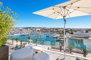 Moderne Terrasse im Hotel Avenida Lagos mit weißem Sonnenschirm, Sitzbereich und Panoramablick über den Yachthafen mit Booten und Palmen.