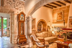 Rustikale Eingangshalle mit Steinwänden, sichtbaren Holzbalken, Rundbögen, Standuhr und klassischen Möbeln im Son Sant Jordi Pollenca.