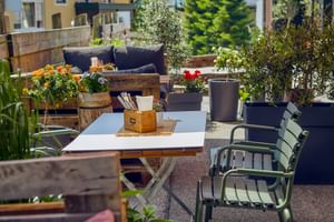 Sunny garden terrace at Hotel Astrid Saalbach with white table, green chairs, colorful flowers in planters, and lounge seating area.