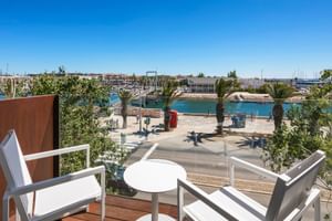 Weiße Balkonmöbel auf Hotel Avenida Terrasse mit Blick auf Lagos Hafen mit türkisfarbenem Wasser, Palmen und Marina mit Booten unter blauem Himmel.