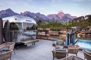 Rooftop terrace at Hotel Sepp Maria Alm with silver Airstream trailer, lounge furniture, pool, and mountain views in Austria.