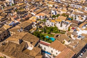 Luftaufnahme von Son Sant Jordi in Pollença mit traditionellen Gebäuden mit Terrakottadächern, einem zentralen Pool umgeben von Gärten und Zypressen.