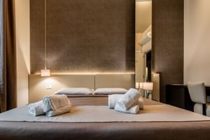 Modernes Hotelzimmer im Palazzo del Garda mit Doppelbett, brauner Textur-Kopfteilwand, Pendelleuchten und ordentlich gefalteten Handtüchern.