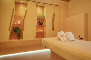 Moderner Massageraum im Hotel Palazzo del Garda mit cremefarbenem Behandlungstisch, weißen Handtüchern und beleuchteten Wandnischen mit Pflanzen.