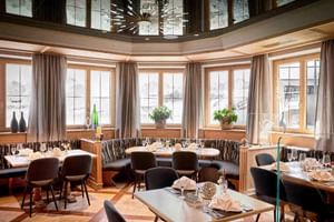 Elegantes Restaurant im Hotel Alte Post Fieberbrunn mit gedeckten Tischen, moderner Leuchte und großen Fenstern mit Bergblick.
