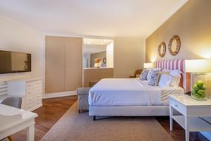 Helles Doppelzimmer mit gestreiftem Kopfteil, weißer Bettwäsche, Holzboden, beigem Kleiderschrank und gelber Akzentwand mit Spiegeln.