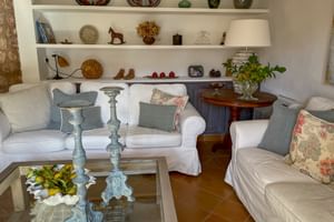 Helle Lounge im Can Quatre Sóller mit weißen Sofas, Zierkissen, Glascouchtisch und weißen Regalen mit Keramik und Dekor.