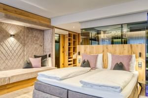 Modernes Doppelzimmer mit zwei Betten, Holzkopfteilen, rosa und grauen Kissen, gepolsterten Wandpaneelen und Holzregalen im Hotel Alte Post Fieberbrunn.