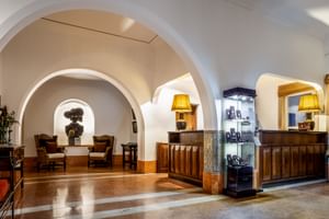 Hotelrezeption im Pousada Sagres mit weißen Gewölbedecken, hölzernem Empfangstresen, gelben Tischlampen und Sitzbereich durch Bogen sichtbar.