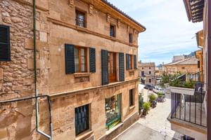 Traditionelles Sandsteingebäude in Pollenca mit grünen Fensterläden und Ziegeldach, mit Blick auf eine ruhige Straße mit mediterraner Architektur.