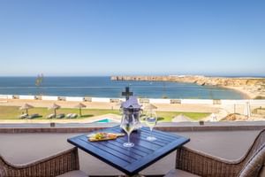 Balkonterrasse mit Champagner und Korbstühlen mit Blick auf Pool, Küstenklippen und Atlantik in der Pousada Sagres, Portugal.